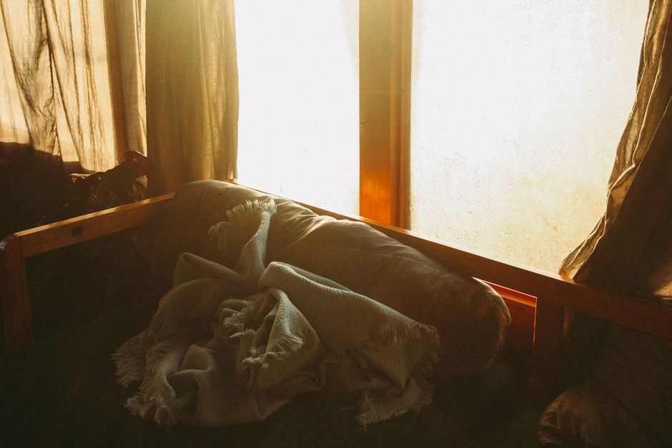Warm and cozy interior scene with sunlight streaming through a window onto a sofa and blanket.